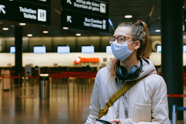 Woman with face mask and headphones at airport, COVID and Travel Insurance concept